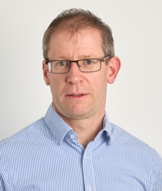 Head and shoulders of Patrick Byrne wearing glasses and a blue and white striped shirt