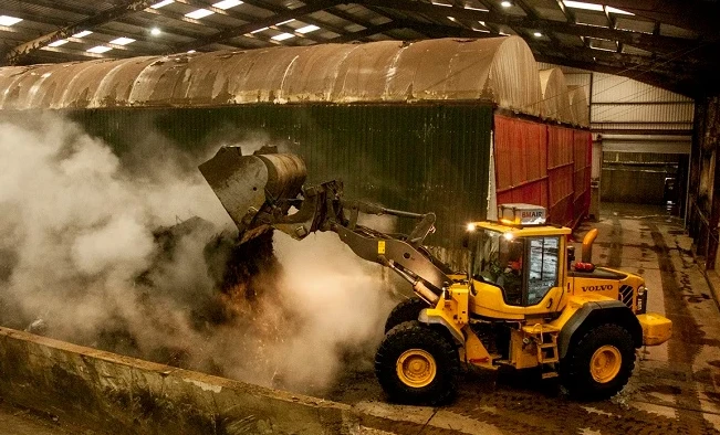 Yellow industrial tractor unloading organic waste for composting