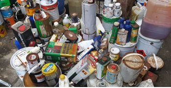 Picture shows some containers of hazardous waste such as varnish, oil, adhesives, paint, and indistinguishable containers with hazardous labels
